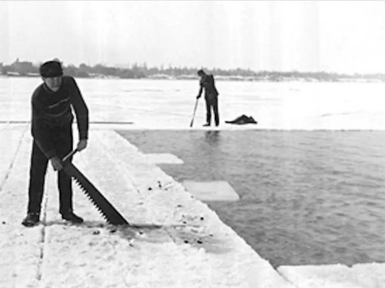 Workers cutting blocks of ice on a frozen lake with long saws