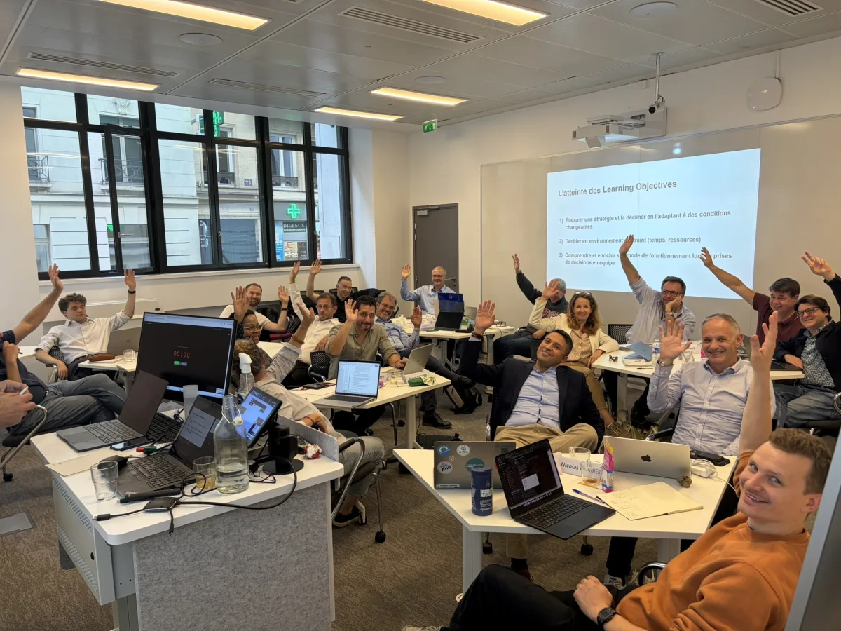 Participants in an Arena64 KRONOS business simulation session, seated in teams with their laptops